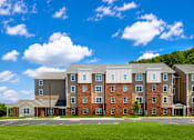 Thumbnail 3 of 15 - A large multi-story apartment building with a green lawn in front.