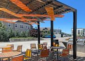 Thumbnail 5 of 8 - A patio with orange chairs and tables under a striped awning.