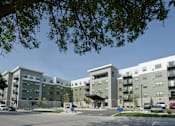 Thumbnail 3 of 7 - A large apartment complex with a parking lot in front.