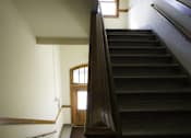 Thumbnail 31 of 100 - A staircase with a wooden handrail and a door at the bottom.