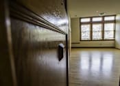 Thumbnail 77 of 100 - A dark wooden door with a handle in the foreground and a brightly lit room in the background.