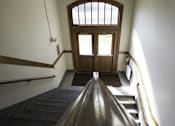Thumbnail 80 of 100 - A wooden staircase with a metal railing and a tiled floor leads to a door with a window above it.