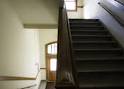 Thumbnail 81 of 100 - A staircase with a wooden handrail and a door at the bottom.