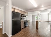 Thumbnail 25 of 29 - A black refrigerator in a kitchen with wooden floors and white walls.