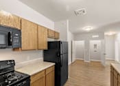 Thumbnail 2 of 16 - A black refrigerator in a kitchen with wooden cabinets.
