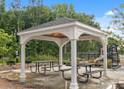 Thumbnail 12 of 16 - A white gazebo with a brown roof is surrounded by picnic tables.