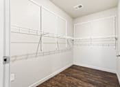 Thumbnail 23 of 32 - A walk-in closet with white shelving and a wooden floor.