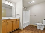 Thumbnail 6 of 27 - A white toilet sits in a bathroom with wood floors and white walls.