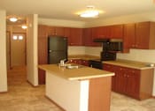 Thumbnail 12 of 18 - A kitchen with wooden cabinets and a black refrigerator.