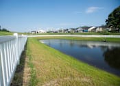 Thumbnail 4 of 25 - A white fence runs along the edge of a grassy field with a pond in the middle.