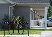 Thumbnail 7 of 25 - A black metal bike rack sits in front of a grey house.