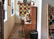 Thumbnail 23 of 33 - A room with a wooden desk and chair, a quilt hanging on the wall, and a window with blinds.