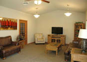 Thumbnail 9 of 18 - A living room with a brown leather couch, a wooden coffee table, and a television.