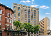 Thumbnail 6 of 8 - A large building with many windows sits in the middle of a city street.
