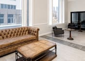 Thumbnail 5 of 8 - A brown tufted couch sits in a living room with a wooden coffee table in front of it.