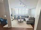 Thumbnail 12 of 12 - A living room with a grey couch, a blue chair, and a white coffee table.