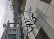 Thumbnail 8 of 16 - A metal bench with a backrest is on a sidewalk.