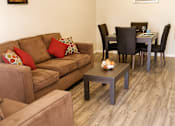 Thumbnail 3 of 9 - A brown couch with red pillows sits in a living room with a dining table and chairs.