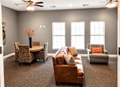 Thumbnail 21 of 46 - A living room with a brown couch, a table with a vase of flowers, and a ceiling fan.