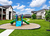 Thumbnail 19 of 46 - A playground with a green and blue slide in the middle of a grassy area.