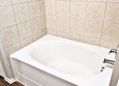 Thumbnail 37 of 46 - A white bathtub is installed in a bathroom with beige tiles.