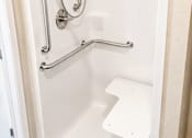 Thumbnail 39 of 46 - A white shower stall with a white seat and silver grab bars.
