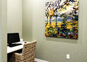 Thumbnail 32 of 46 - A painting of a forest scene is hanging on a wall above a desk with a computer.