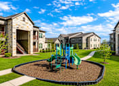 Thumbnail 7 of 46 - A playground with a green slide and a blue swing set in the middle of a gravel area.