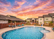 Thumbnail 1 of 23 - A swimming pool surrounded by a wooden fence and benches with a sunset in the background.