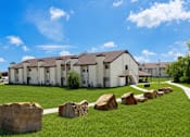 Thumbnail 1 of 5 - A row of houses with a grassy front yard and large rocks in the foreground.