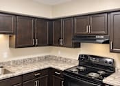 Thumbnail 12 of 17 - A kitchen with dark brown cabinets and a black stove top oven.