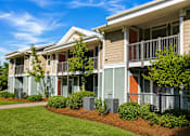 Thumbnail 13 of 14 - A row of townhouses with green lawns and bushes in front.