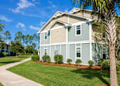 Thumbnail 14 of 14 - A house with a green and beige exterior is surrounded by a well-manicured lawn and a clear blue sky.