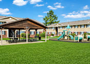Thumbnail 2 of 9 - A playground with a green slide and picnic tables in front of a building.