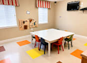 Thumbnail 9 of 9 - A white table surrounded by colorful chairs in a room with a television on the wall.