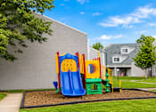 Thumbnail 3 of 9 - A playground with a slide and a climbing frame is in front of a grey building.