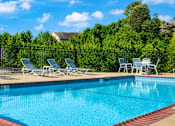 Thumbnail 7 of 9 - A pool with blue water and white chairs around it.