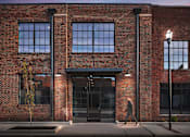 Thumbnail 5 of 9 - A person is walking in front of a red brick building.
