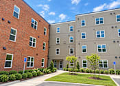 Thumbnail 1 of 13 - A building with a red brick exterior and a building with a tan exterior.