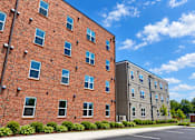 Thumbnail 3 of 13 - A red brick building with a parking lot in front.