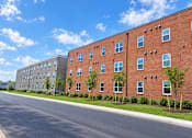 Thumbnail 2 of 13 - A long brick building with a tree in front of it.