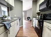 Thumbnail 20 of 26 - a kitchen with white cabinets and black appliances and a hallway with a fireplace