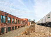 Thumbnail 7 of 9 - A train is passing by a row of red brick buildings.