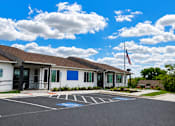 Thumbnail 5 of 12 - A building with a flag on the right side and a parking lot in front.