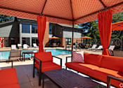 Thumbnail 23 of 26 - A poolside seating area with red cushions and umbrellas.