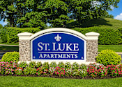 Thumbnail 1 of 4 - A sign for St. Luke Apartments is surrounded by flowers and greenery.