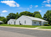 Thumbnail 4 of 4 - A white building with a grey roof is surrounded by a parking lot.