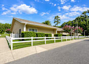 Thumbnail 4 of 5 - A house with a white fence and a driveway in front.