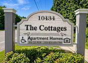 Thumbnail 2 of 5 - A sign for The Cottages Apartment Homes with a phone number and TTY number.