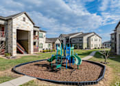 Thumbnail 8 of 23 - A playground with a green slide and a brown sandbox in the middle of a grassy area.